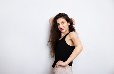 Happy relaxing toothy smiling make-up woman with red lipstick, long brown hair standing in black top near the wall on empty copy space studio blue background. Portrait