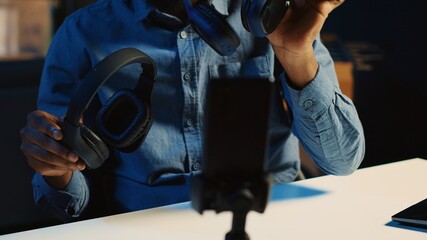 Content creator in dimly lit living room filming video review of noise cancelling headphones...