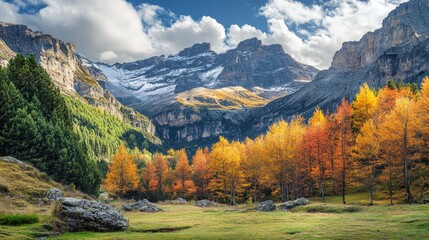 Fototapeta premium A valley in the Pyrenees mountains with a forest in the foreground, with a mix of green and orange trees, and snow-capped peaks in the background under a cloudy sky.