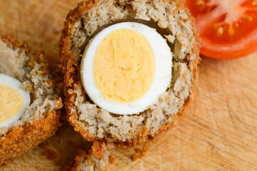 Traditional Scotch Egg,close-up and cut into two half segments,being prepared on a domestic kitchen wood bread board.