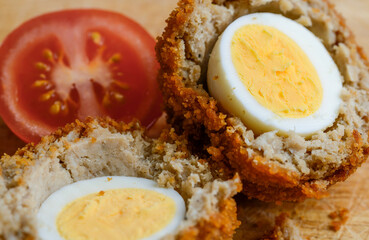 Traditional Scotch Egg,close-up and cut into two half segments,being prepared on a domestic kitchen wood bread board.