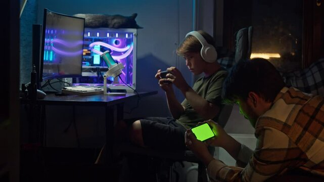 Older and younger brothers are playing a cross-platform game together on their phone and gaming PC, sitting in the same room. Chromakey