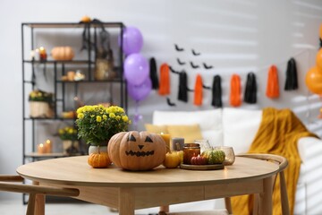 Halloween celebration. Pumpkin with creepy face, candles and flowers on wooden table in decorated room