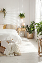 Stylish bedroom interior with large bed, houseplants and decorative elements