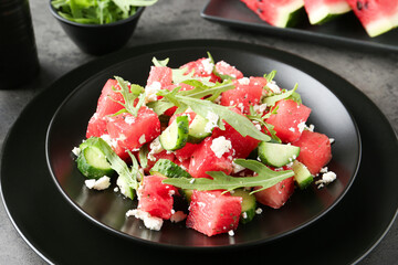 Delicious watermelon salad with feta cheese, cucumber and arugula on grey table, closeup