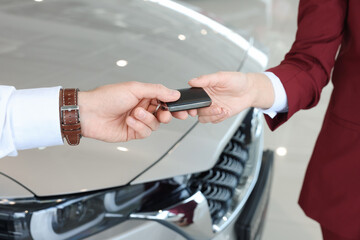 Fototapeta premium Salesman giving key to client near new car in salon, closeup