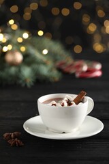 Tasty hot cocoa drink with marshmallows in cup and spices on black wooden table
