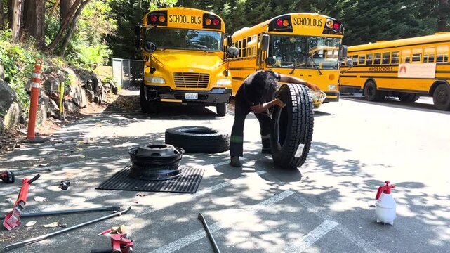 Latino man in uniform provides maintenance and tire repair service to school buses