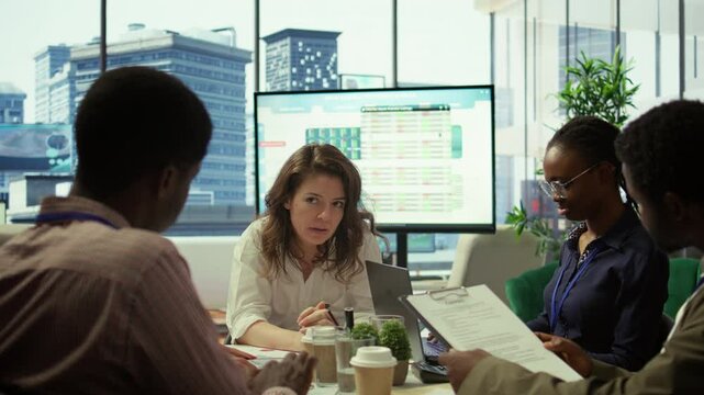 Financial expert showing statistics data on papers in a conference room, briefing meeting with staff for a presentation. Coworkers studying sales reports to adapt within market needs. Camera B.