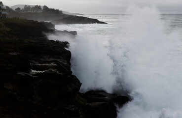 Fototapeta premium Ocean Wave Crashing Into Dark Rock Shore Overcast Sky