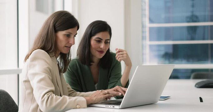Two businesswomen using laptop in boardroom discuss business-related matters. Analyze sales performance and strategies to boost revenue, review market research data, planning upcoming business project