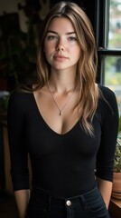 Fototapeta premium A captivating brunette gazes thoughtfully out a window, her silver necklace glimmering against a dark top.