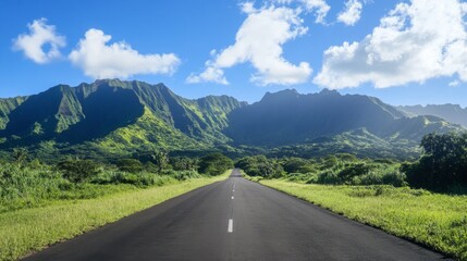 Naklejka premium A straight asphalt road leading into lush green mountains, with a clear sky and scattered clouds on a bright, sunny day.