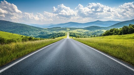 A straight asphalt road leading towards green mountain scenery, with a sunny sky and gentle, fluffy clouds on a bright day.
