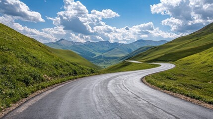 Naklejka premium A winding asphalt road with green mountains on either side, under a bright sky and scattered clouds on a sunny afternoon.