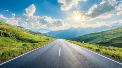 An asphalt road stretching through green mountain valleys, with a bright sky and fluffy clouds on a sunny afternoon.