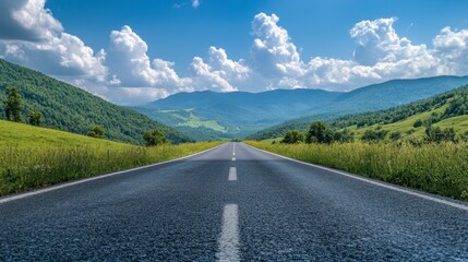 An asphalt road stretching towards green mountains, with a bright blue sky and puffy clouds on a sunny, clear day.