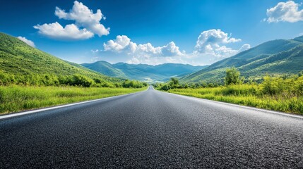 An asphalt road stretching towards green mountains, with a bright blue sky and puffy clouds on a sunny, clear day.