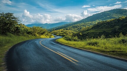 Naklejka premium An asphalt road through lush green mountain landscapes, under a bright sky with soft, scattered clouds on a sunny afternoon.