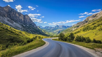 Naklejka premium An asphalt road winding through green mountain valleys, with a clear blue sky and scattered clouds on a sunny day.