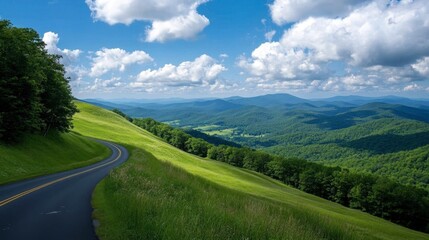 Naklejka premium An asphalt road winding through green mountain valleys, with a clear sky and soft white clouds on a sunny, bright day.