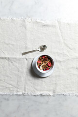 overhead view of small white bowl of homemade granola containing dried fruit, nuts and seeds with a sterling silver spoon on a piece of rough edge light beige linen