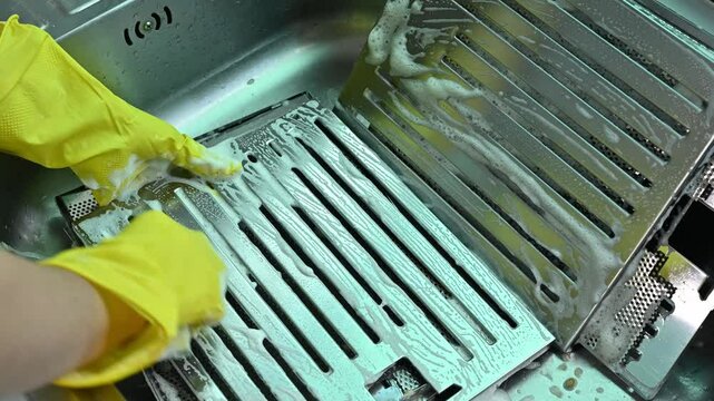 Someone hands using sponge to cleaning a cooker hood filters at kitchen sink. Clean your filters every two to three months, depending on your cooking habits.