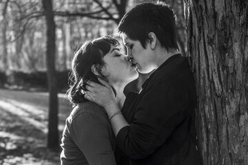 LGBT couple of women sharing a passionate kiss against a tree in black and white