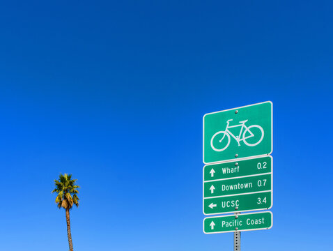 Green bicycle route sign points to local destinations in Santa Cruz, California, including the Wharf, Downtown, UCSC, and the Pacific Coast