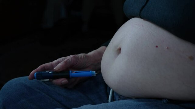 Mature adult carefully injecting diabetes medication into large, exposed abdomen. Empowering self-care and self-management for aging population.