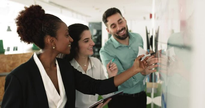 Marketing department, African and Latin teammates working on joint task check information presented on white board, share ideas, make strategic plan, forecasting, take part in teamwork in workplace