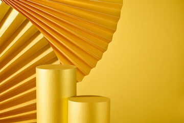 A classical mood is created against a bronze-gold backdrop by encircling two cylindrical golden platforms that are utilized for product display with paper fans.