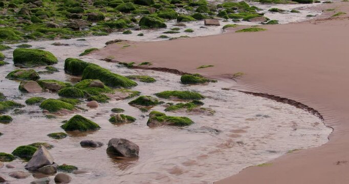 wide shot of Water from Rottington beck flowing onto the beach at Saint bees seafront at low tide, West lake district. West lake district