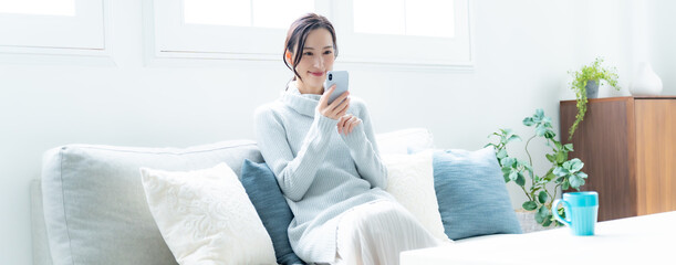 リビングのソファで携帯を持つ笑顔の女性