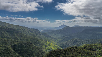 Beautiful mountain landscape. The mountain slopes are covered with lush tropical vegetation. Peaks against a blue sky and clouds. Mauritius. Observation deck, Black River Gorges National Park 