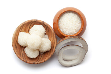 Top view of fresh coconut fruit pieces and coconut shreds in a ceramic pot, with laddu isolated on a white background.