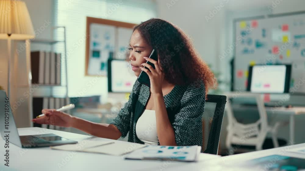 Aufkleber Woman multitasking at work, discussing on the phone while examining documents and using a laptop in a modern office setting