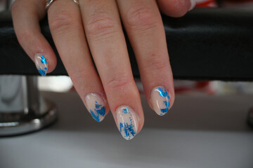 Woman hand with fresh gel polish and blue nail art design, resting on a black leather armchair in a beauty salon