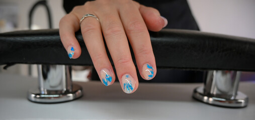 Woman hand with fresh gel polish and blue nail art design, resting on a black leather armchair in a beauty salon