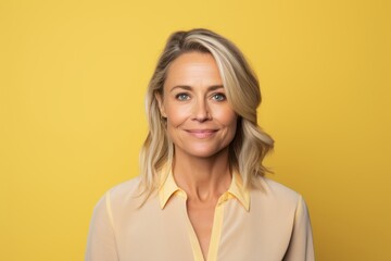 Portrait of a beautiful middle aged woman with blond hair smiling at the camera over yellow background
