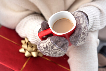 Close-up of hands in knitted mittens with a red mug of hot coffee.