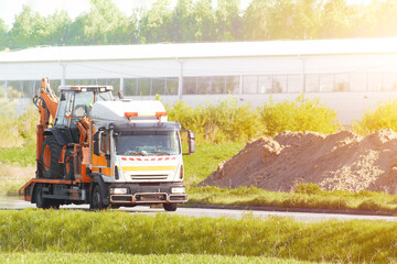 Tow truck transporting excavator on countryside road during summer day