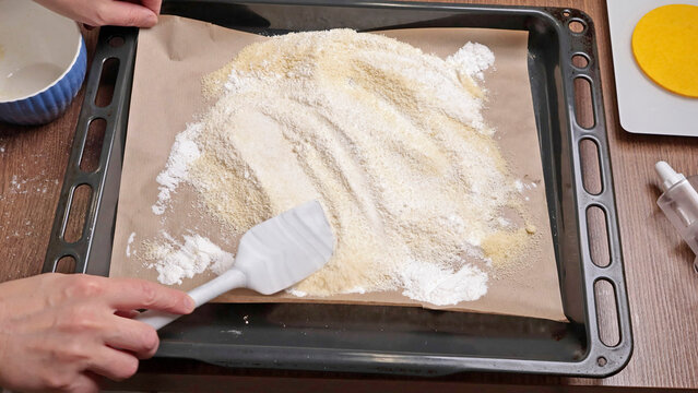 The process of making dough. Woman mixes powdered sugar and almond flour with silicone spatula on tray in kitchen. Baking macarons at home. Hands close-up.
