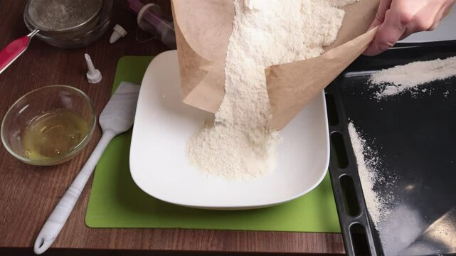 Process of making dough. Woman pour mixture of powdered sugar and almond flour into bowl in kitchen. Baking macarons at home. Hands close-up.