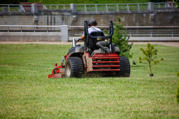 A person operating a lawn mower in a park, cutting the grass. The person is wearing a hat and headphones, focused on the task at hand