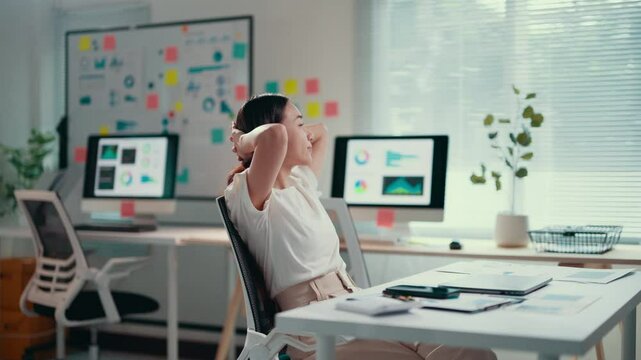 Young businesswoman working on a laptop in a modern office takes a break to stretch, promoting well-being and productivity in a dynamic work environment