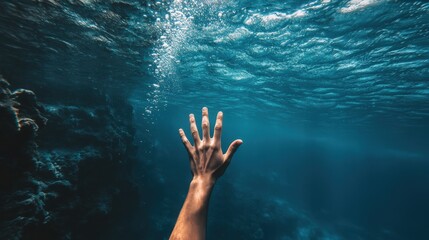 Underwater vertical shot of a diver reaching toward the surface with one hand