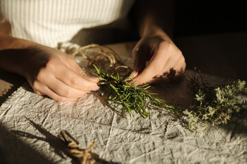 Woman uses natural twine to tie rosemary sprigs. Preparing fresh herbs for drying and spice use