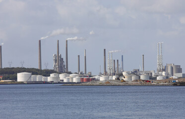 industrial plants and silos in a large industrial area near the sea with white polluting rising...