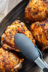 Fried chicken with hot thai bbq seasoning on a black stoneware dish with kitchen tongs. On wooden background